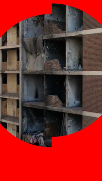 A drone shot of the side of an abandoned building. The facade is covered in cloths providing protection for some of those living inside.