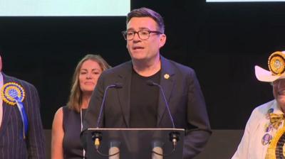 Andy Burnham standing on stage in Wigan