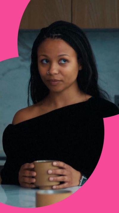 Industry character Harper looks to the side while holding a mug on a table. She has long black hair and wears a black top