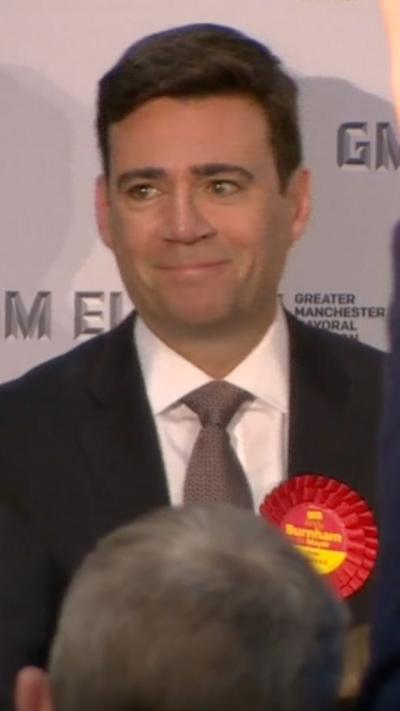 Andy Burnham pictured - a man with dark hair wearing a black suit and wearing a labour badge.