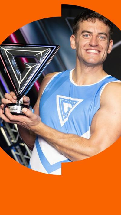 Josh McDonald has short black hair. He is wearing a blue Gladiators singlet and holding the Gladiators trophy.