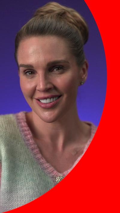 Danielle Lloyd smiles wearing a multicoloured cardigan; she has brown hair tied in a bun