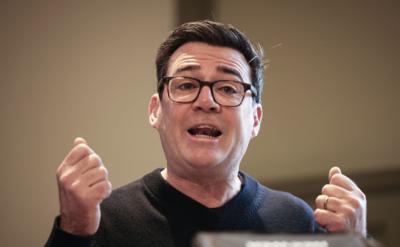 Andy Burnham has short dark hair and wears glasses and a black top