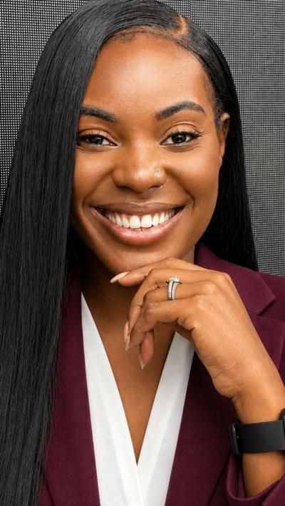 A black woman with long straight black hair smiling wearing a burgundy jacket over a white blouse