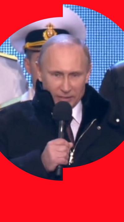 A man with short hair stands on stage and speaks into a microphone
