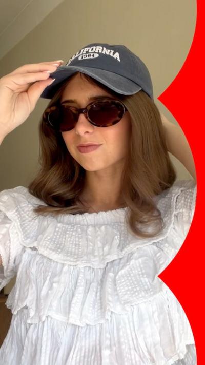 A young woman wearing a white top, sunglasses and a navy cap.