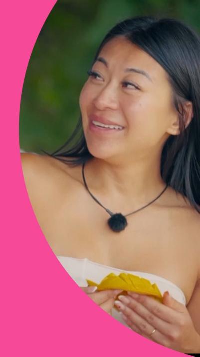 A woman eats a mango. She has long black hair and wears a low-cut white top