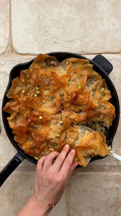 Courgette and pistachio filo pie in a pan with a portion being taken out on a serving spoon