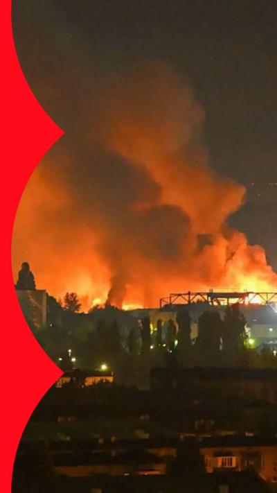 Large fire burning at night behind buildings and trees
