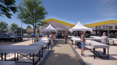 Long white tables set out on an outdoor concourse, with white gazebo-style shelters. A building lies in the background with double-pitched roof. There is car parking to the left.