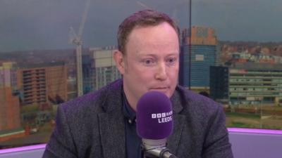 A man in a BBC Radio Leeds studio behind a purple microphone