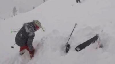 A rescuer is rescuing a skier that is under the snow.