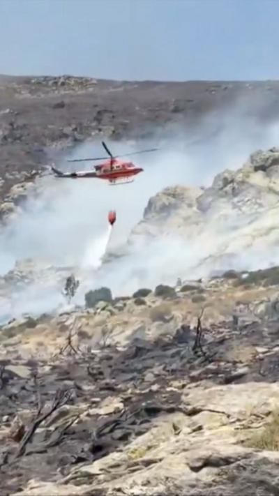 Red firefighter helicopter drops water onto a smouldering hillside.