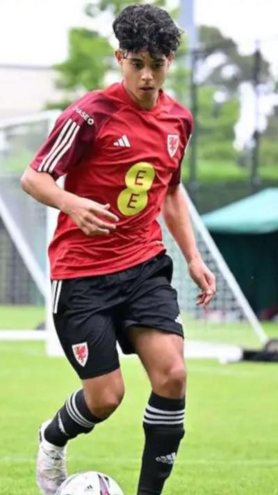A teenager in a Wales football kit dribbling a ball