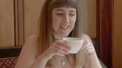 A woman with bare shoulders drinks a cup of tea