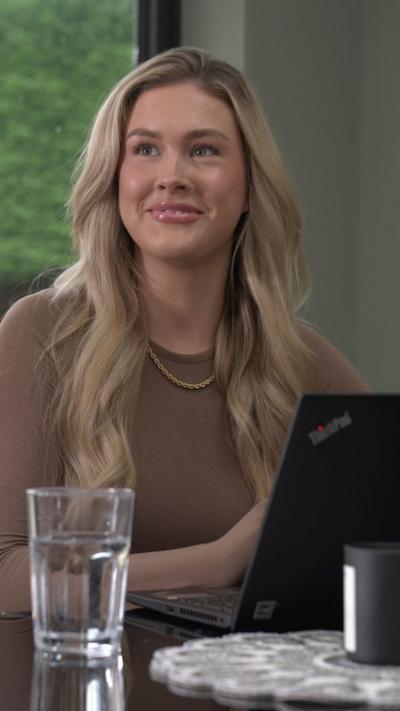Blonde woman smiles looking to left of camera, in front of a glass of water. 