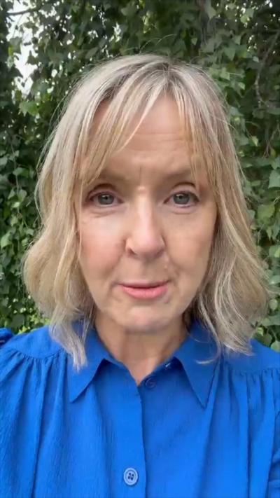 Tara Mills has shoulder length blonde hair, she is wearing a dark blue shirt. 