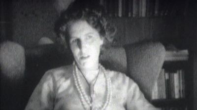 A woman wearing pearls sitting in her home.