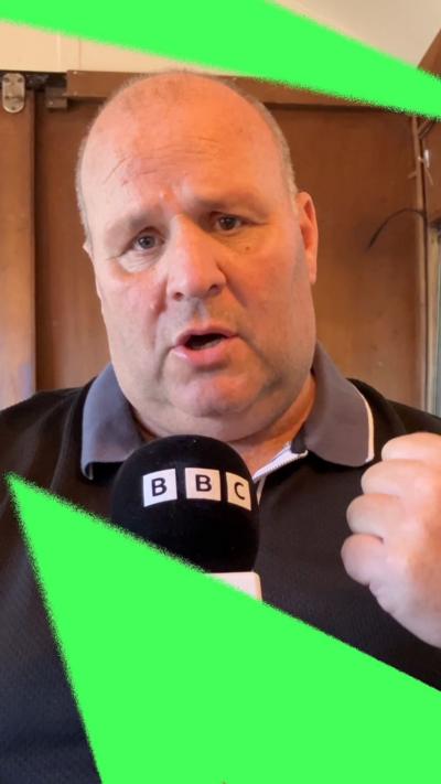 Big John holding a BBC microphone and holding his fist in the air