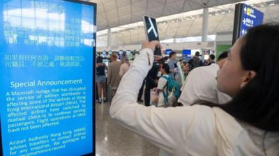 A woman takes pictures of an announcement about the Microsoft outage at Hong Kong International Airport in Hong Kong, China