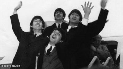 The members of The Beatles wave to fans as they disembark a plane.