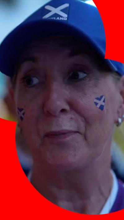 Woman wearing a blue cap with the Scotland flag on the front. She has a two heart-shaped Scotland flags painted on her face.