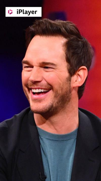 Actor Chris Pratt smiles - he has short brown hair and wears a dark jacket