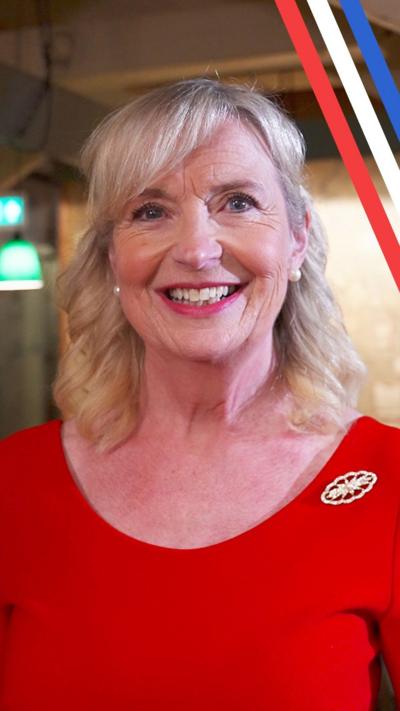 Carol Kirkwood, wearing a red dress and brooch, smiling in the map room of Churchill's War Rooms