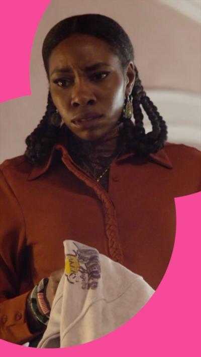 A woman with long dark hair and an dark orange top looks serious