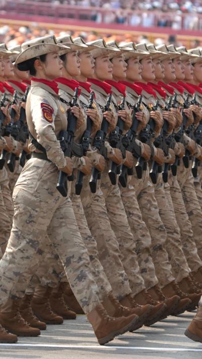 Dozens of soldiers walk in line holding guns at the military parade