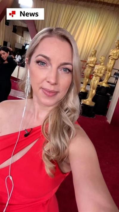 A woman, Emma Vardy, wears a red dress and she stands on the red carpets in Hollywood.