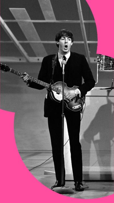 A black and white photo of Paul McCartney playing his bass in the 19060s