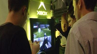 Men standing around a screen showing an Xbox game