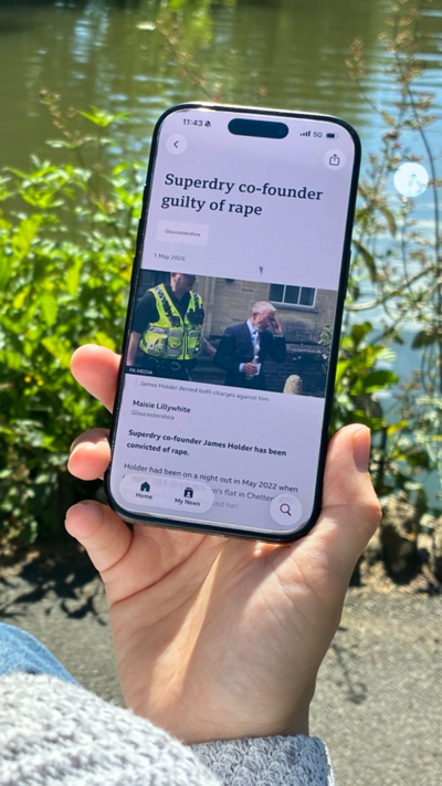 Hand holding a phone displaying article about James Holder being found guilty of rape. A body of water is in the background.