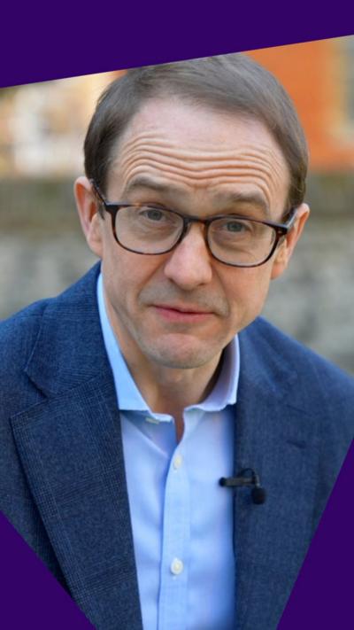 A close up shot of BBC political editor Chris Mason, wearing dark glasses, a blue shirt and blazer