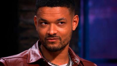 A man, Steven Bartlett, gives a side-eye look; he has short black hair and wears a maroon jacket