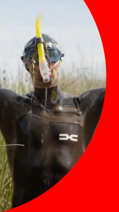 Man in a wetsuit and a mask and snorkel stands with water dripping off him