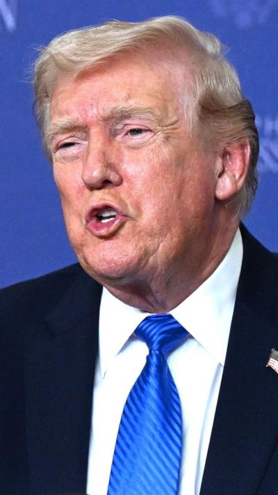 Donald Trump speaks to a crowd wearing a blue tie, white shirt and blue suit.