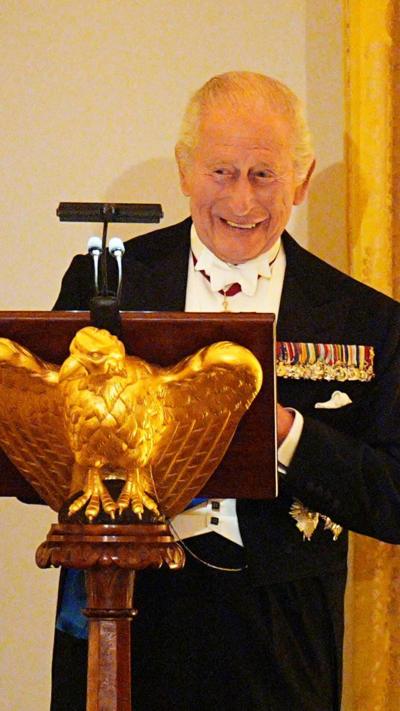 King Charles, stood behind a lectern, dressed formally with medals on his breast, smiles