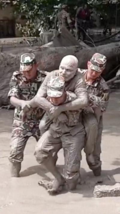 A man covered in mud is carried by soldiers.