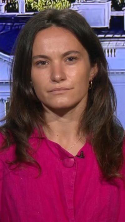 Ione Wells looks into the camera wearing a red top. 