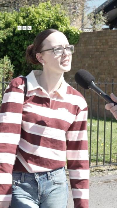 A young woman in a striped red and pink top speaking into a microphone