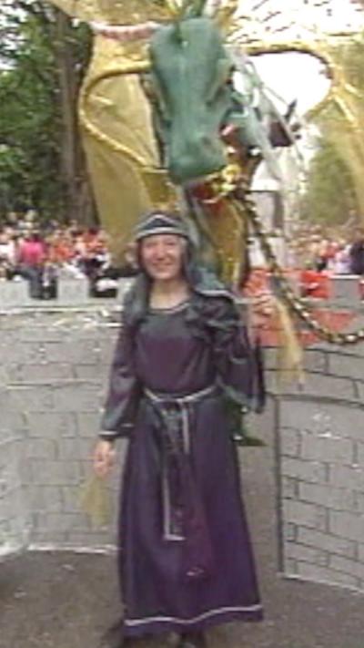 Archive video show a woman in an arabian-like purple costumer with a green and gold dragon's head over her shoulder
