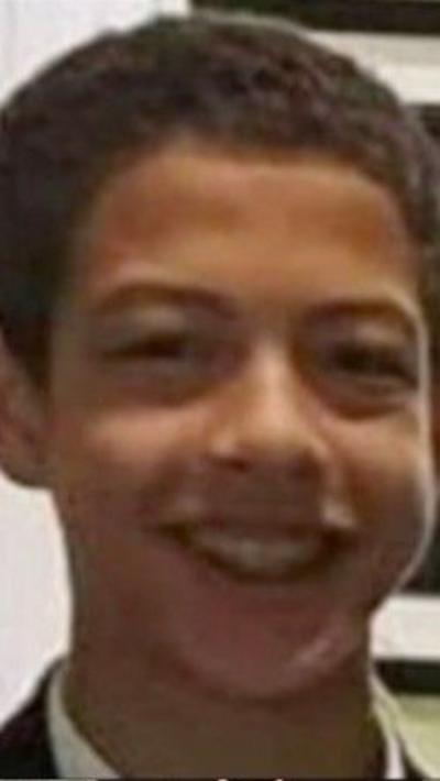 Noah Donohoe is smiling into the camera. He's wearing his school uniform. A framed picture is on the wall behind him.