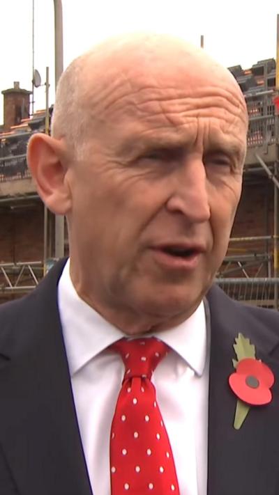 Defence Secretary John Healey. He is wearing a suit with a red tie and a memorial poppy.