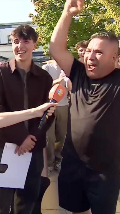 An excited father, stood beside his son, punches the air in celebration.