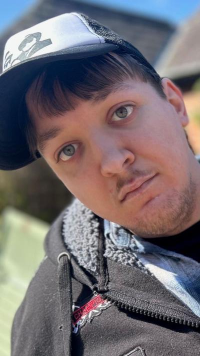A young man wearing a baseball cap and wearing a grey hooded top and blue shirt