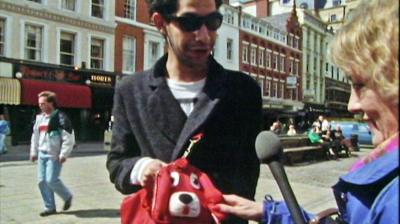 A man in St Ann's Square, Manchester showing Esther Rantzen his dog-shaped handbag.