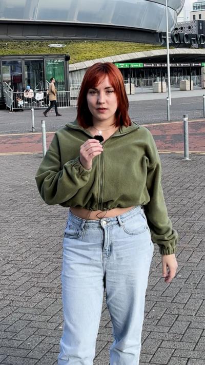 Frankie Allan - woman with shoulder length red hair, dressed casually and holding a microphone in front of the Glasgow Hydro