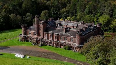 Birds-eye view of a vast Edwardian castle surrounded by trees and greenery.